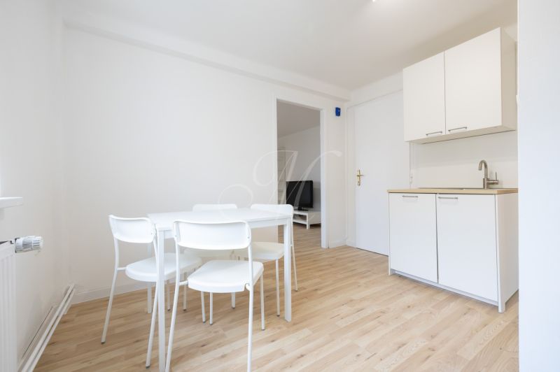 Dining area with a white table and chairs in a 2-room apartment, floor with wood decor.