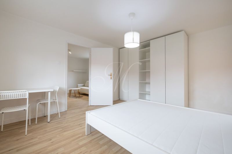 A room of a 2-room apartment with white furniture, a bed, and a floor with a wood decor.