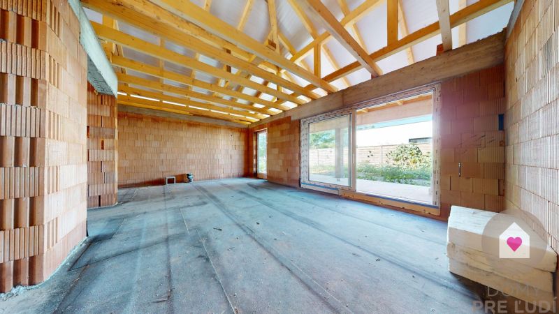 The interior of a partially constructed family house with a roof and large windows, visible bricks.