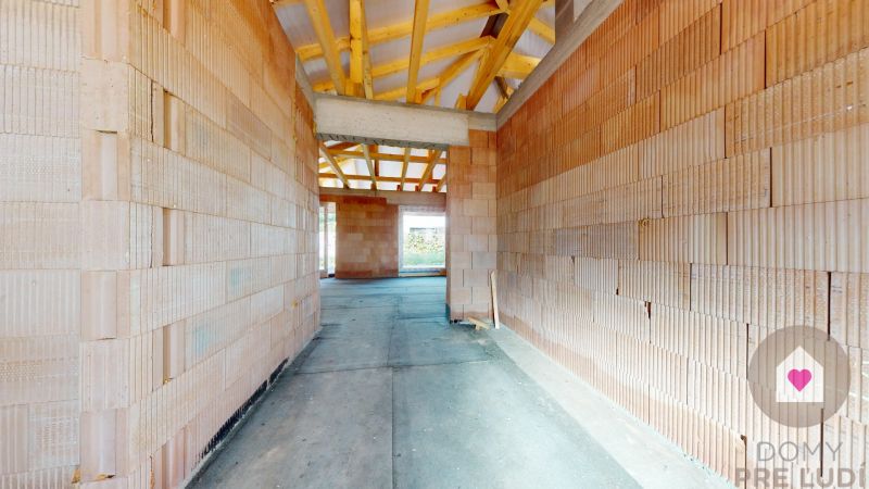 An unfinished interior of a family house with brick walls and visible wooden roof structure.