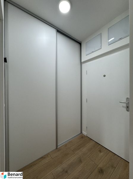 Entrance hallway of a one-room apartment with white sliding doors and a wooden decor floor.
