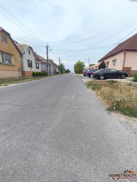 A street in Mikušovce with family houses and parked cars on both sides.