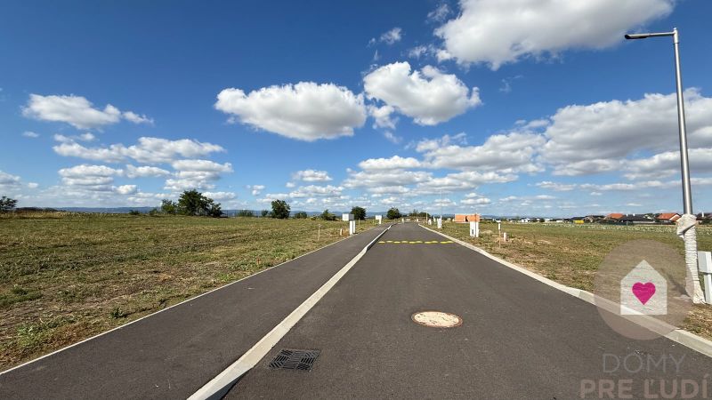 The road on Bernolákova Street in Nová Dedinka surrounded by meadows and a sky with clouds.