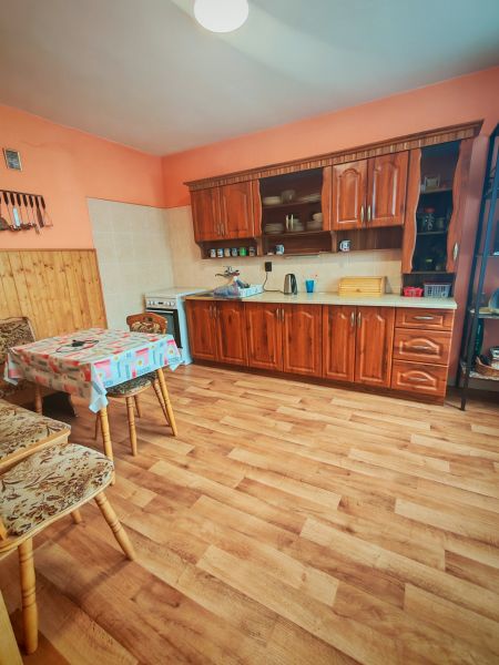 A kitchen in a family house with a wooden decor floor, a wooden kitchen unit, and a table with chairs.
