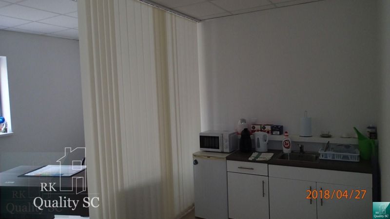 Office kitchenette with appliances, cabinets, and vertical blinds.