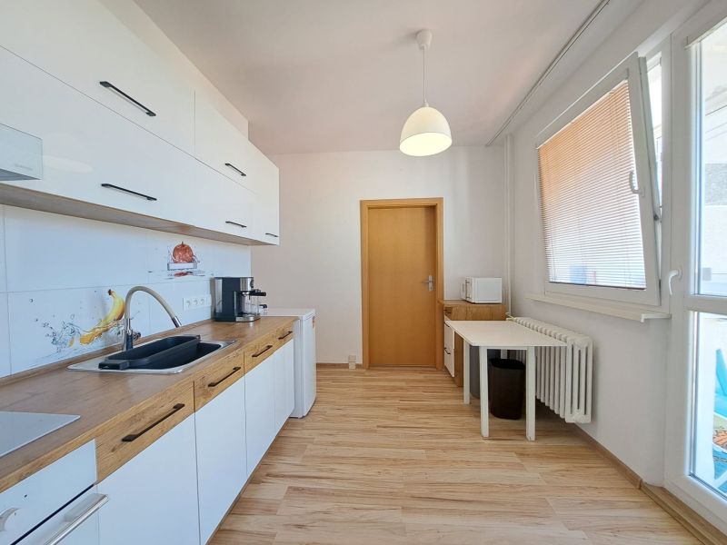 A kitchen in a 3-room apartment with a wooden decor floor and white cabinets.