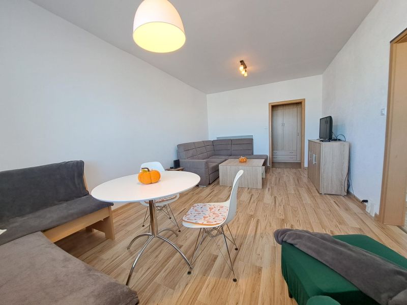 Living room of a three-room apartment with a wooden decor floor, light furniture, and sofas.