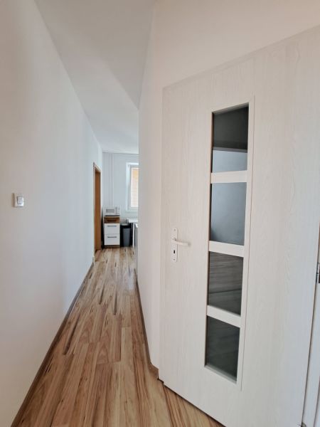 A hallway with light walls and a wooden decor floor in a 3-room apartment.