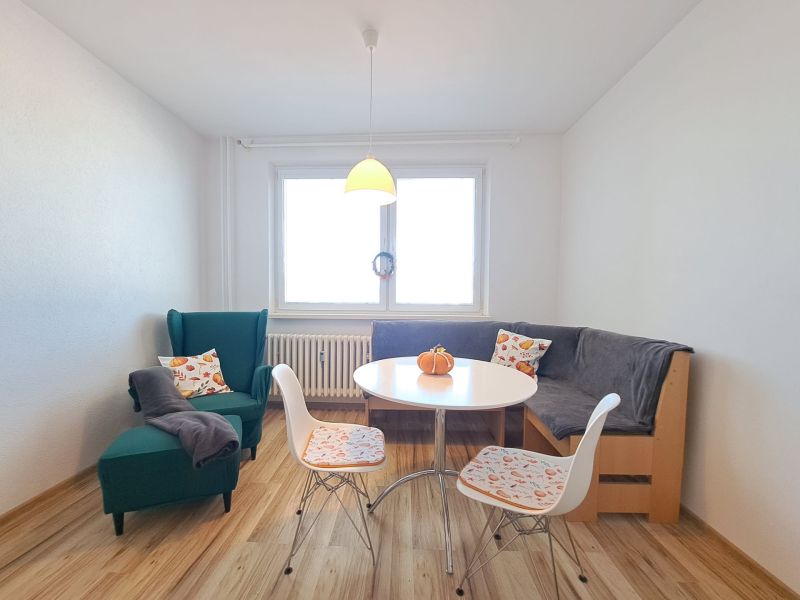 Dining room with an armchair, corner bench, table, and floor with wood decor in a 3-room apartment.