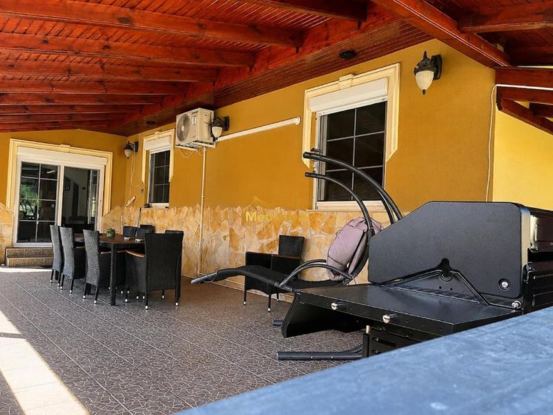 The terrace of a family house in Darnózseli with rattan furniture and a grill under a wooden ceiling.