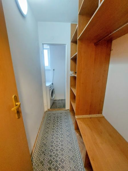 A narrow hallway with built-in wardrobes and a view of the washing machine in a 2-room apartment.