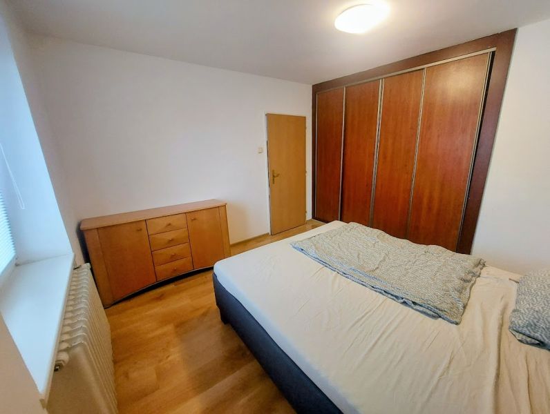 A bedroom with a bed, a large wardrobe, and a floor with a wooden decor in a 2-room apartment.