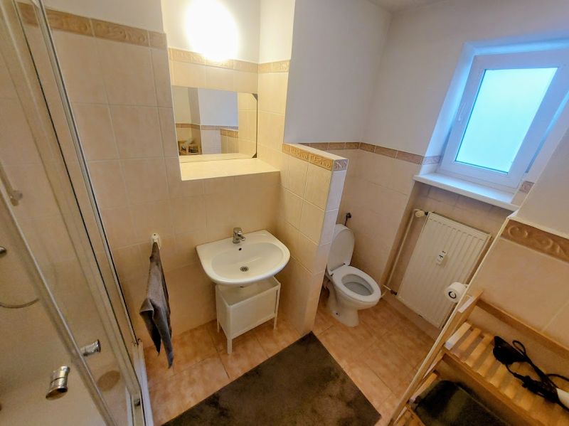 Bathroom of a 2-room apartment with tiles, a shower, a sink, and a window.
