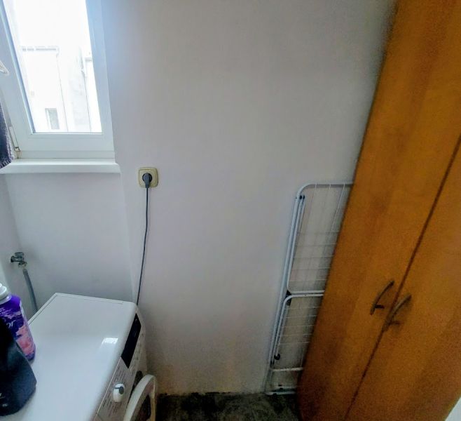 Washing machine next to the cabinet in the bathroom of a two-room apartment with dim lighting.