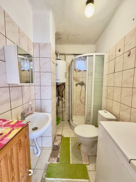 Bathroom with tiles, shower, sink, washing machine, and toilet in a family house.