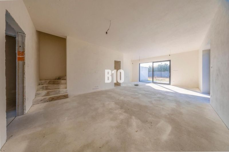 A spacious interior in a family house with bare concrete surfaces and large windows.