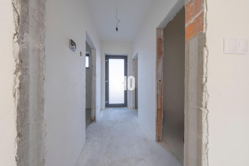 Unfurnished hallway of a family house with white walls and a cement floor.
