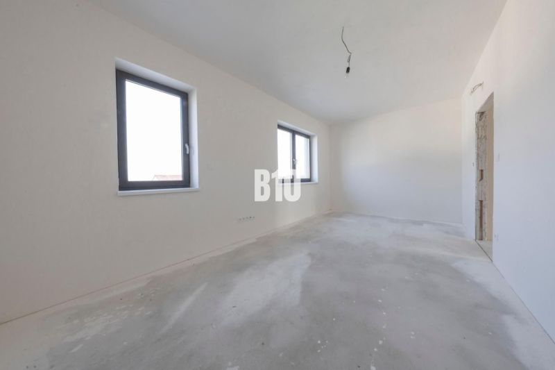 Empty room with two windows and an unfinished floor in a family house.