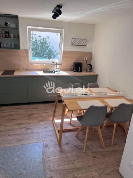 The cottage has a kitchen with wooden decor on the floor, a large window, and a dining table.