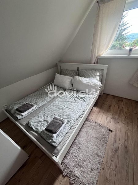 A bedroom in a cabin with a bed, wooden decor flooring, and a window.