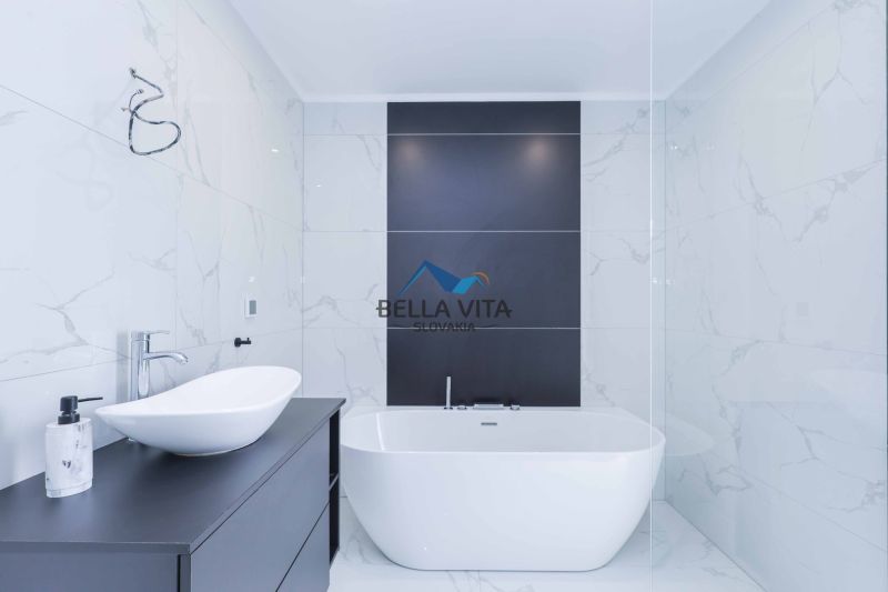 A bathroom in a family house with a freestanding bathtub and black tiles on the wall.