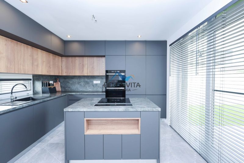 A kitchen in a family house with modern cabinets and large windows with blinds.