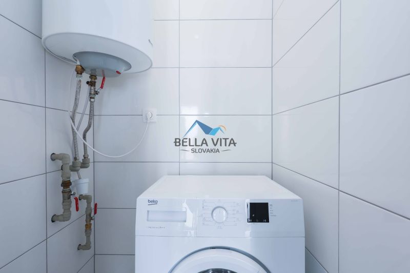 A washing machine and a boiler in the bathroom of a family house with white tiles.