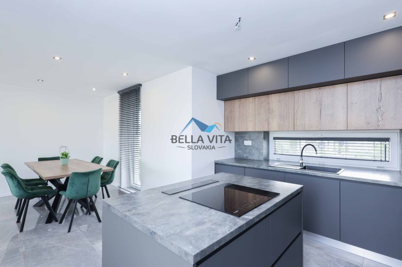 A kitchen in a family house with a kitchen unit and a dining area with green chairs.