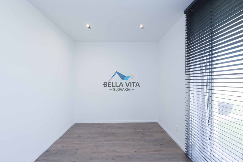 An empty room with wood-patterned flooring and large blinds in a family house.