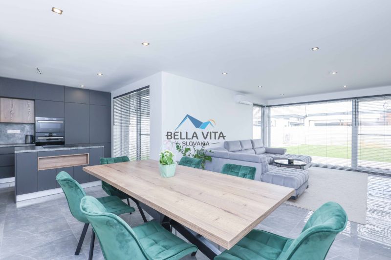 A family house with a kitchenette, a gray sofa, green chairs, and a wooden-patterned floor.