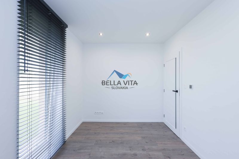 A room with white walls, dark blinds, and a wood-patterned floor in a family house.
