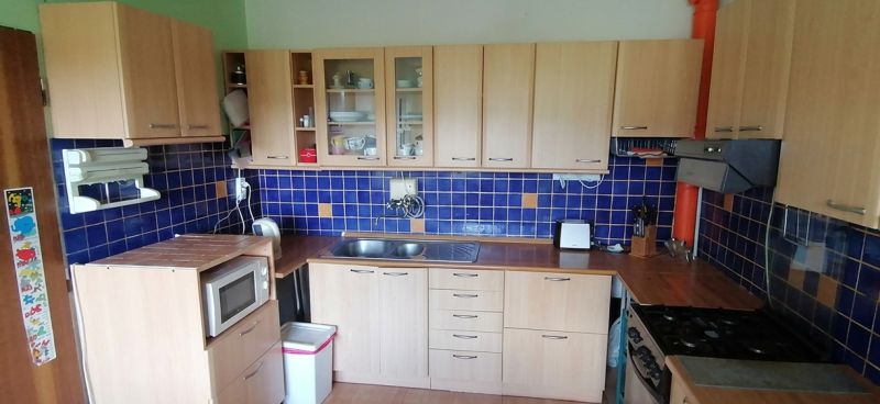 A kitchen in a family house with wooden cabinets, blue tiles, and white appliances.