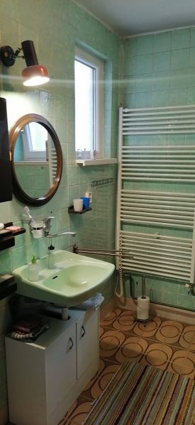 A bathroom in a family house with traditional green tiles on the wall, a mirror, and a sink.