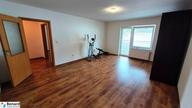 A room in a 3-room apartment, wooden decor flooring, exercise machines, open doors.