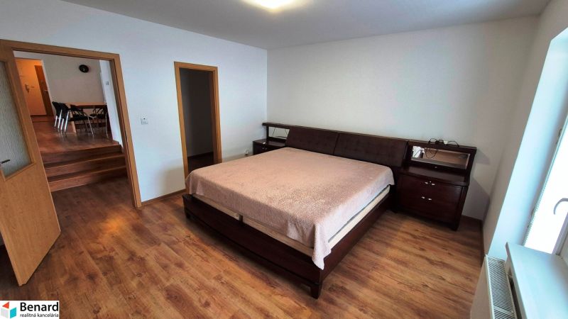 A bedroom in a three-room apartment with a bed, dark furniture, and a floor with a wood decor.