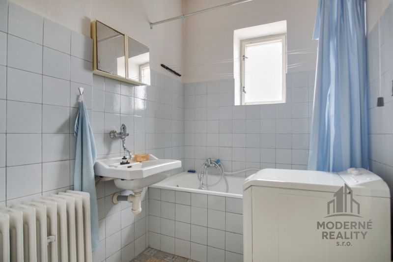 Bathroom in a family house with light tiles, a bathtub, and a washing machine.