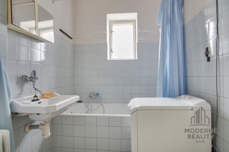 Bathroom with a bathtub, sink, washing machine, and blue shower curtain in a family house.
