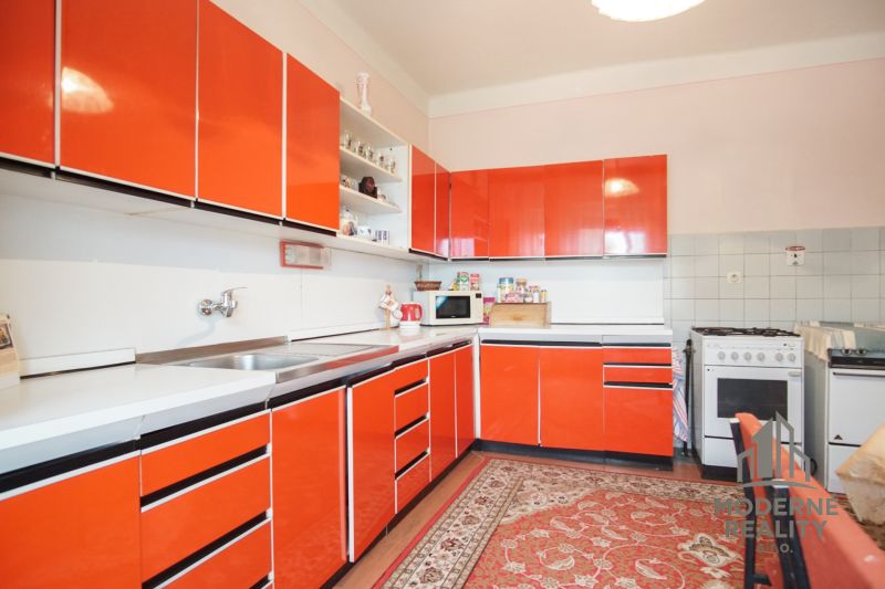 A kitchen with striking orange cabinets and a carpet in a family house.