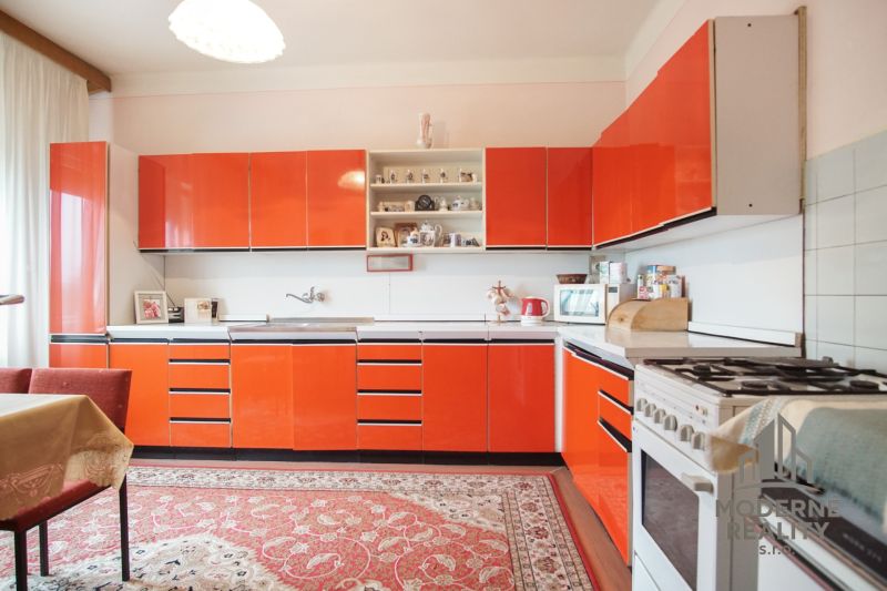 A kitchen with red cabinets and a carpet in a family house.