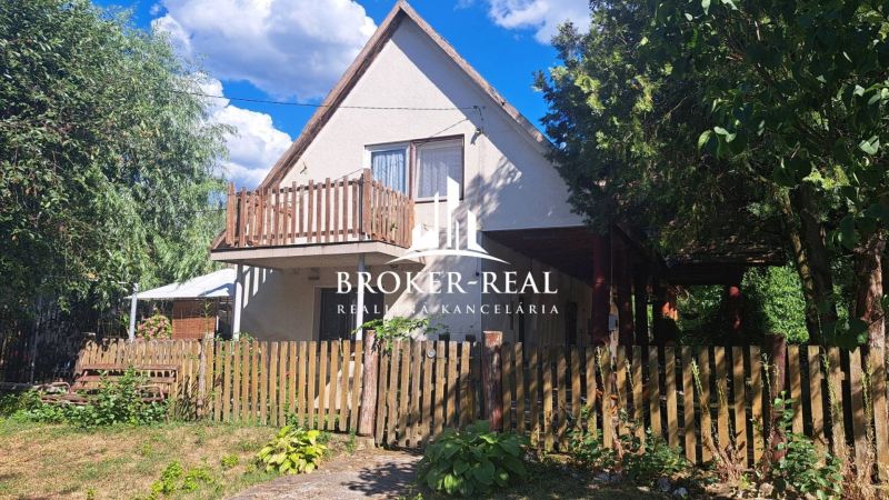 A cottage in Abaújkér with a wooden fence and abundant greenery in the garden.