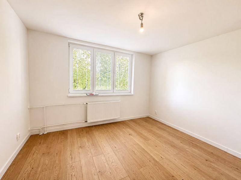A white room in a 3-room apartment with wood-patterned flooring and a window.
