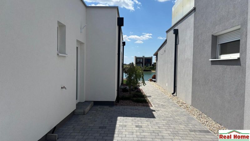 A passage between family houses in Boldog with flowers and a view of the water surface.