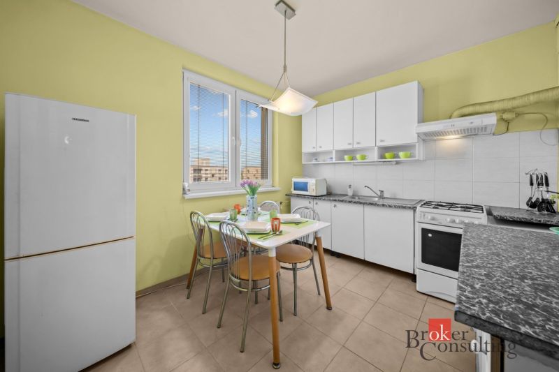 A kitchen in a 3-room apartment with a dining table, white cabinets, and appliances.