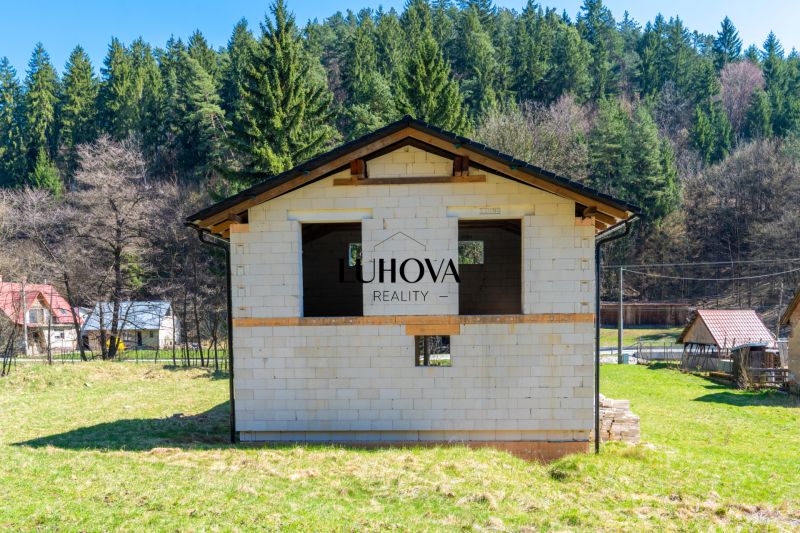 A family house in Lazy pod Makytou surrounded by a forest and other houses on a green plot.