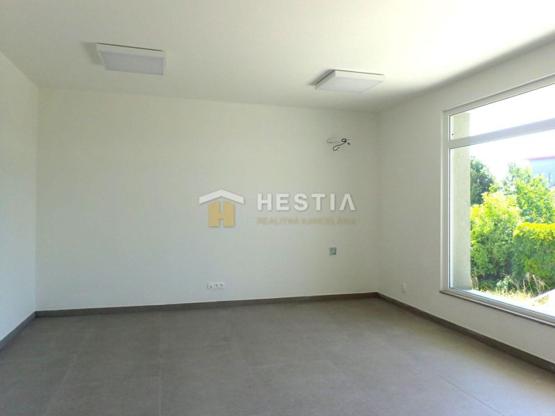 A spacious room with a large window, light-colored walls, and a floor with a wooden decor.