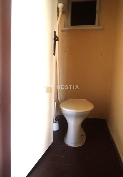 A toilet in a family house with a dark floor and a small window.