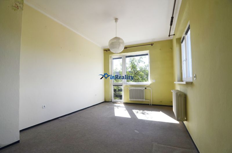 A room in a family house with light walls, a radiator, a large window, a hanging lamp.