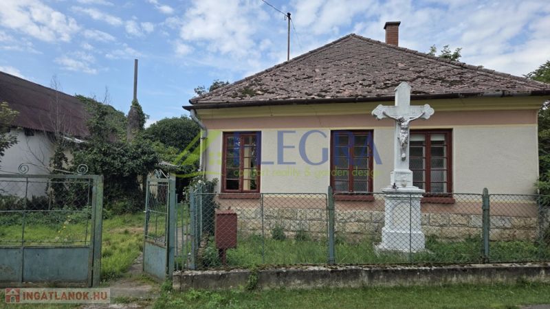 A family house in Boldogkőújfalu with a simple facade and a stone cross in the garden.