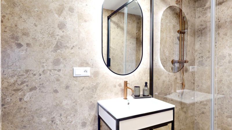 Bathroom of a 3-room apartment with stone tiles, a mirror, and a sink in a black frame.