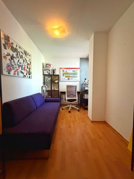 A room in a two-bedroom apartment with a purple sofa and a wooden decor floor.